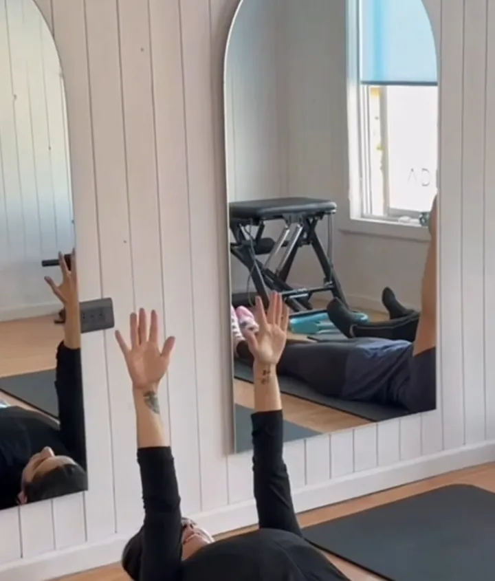 Clase de Pilates: alumnas tendidas con los brazos hacia el techo frente a los espejos arqueados